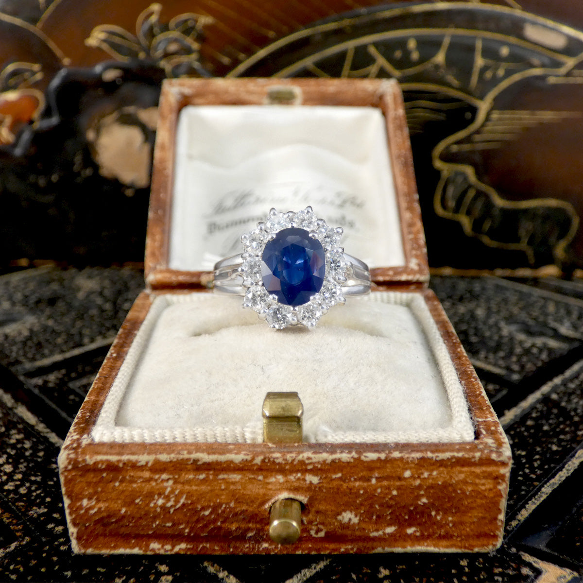 Diamond ring with a blue gemstone in a wooden box on a decorative background