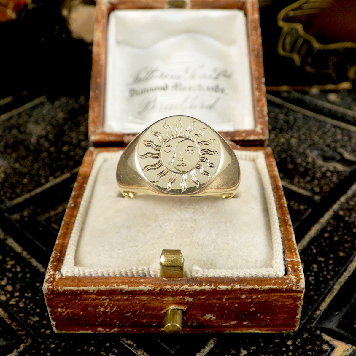 A solid yellow gold signet ring with a face engraved with a sun and moon displayed in a vintage box.