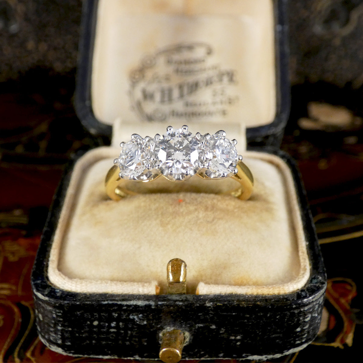 Gold ring with diamonds in an open jewelry box on a patterned fabric background