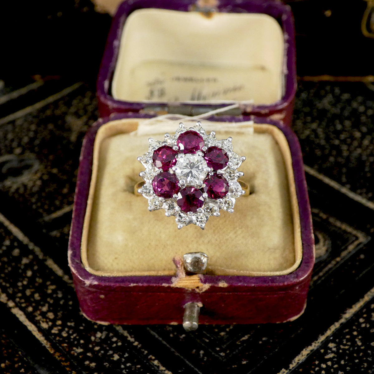 Vintage ring with red gemstones and silver accents in an open purple jewelry box.