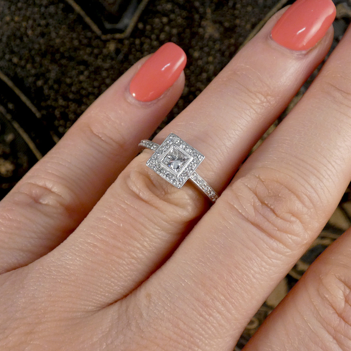 Silver ring with a diamond on a finger with coral nail polish.