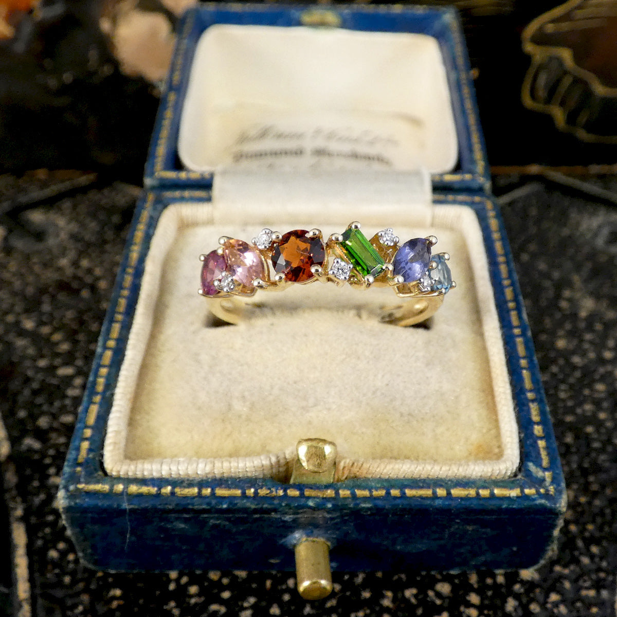 Multicolored gemstone ring in a blue velvet box on a textured surface