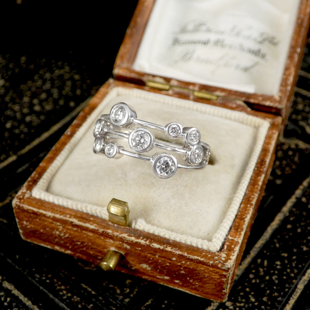 Bubble style diamond ring in Platinum in an open jewelry box on a textured surface