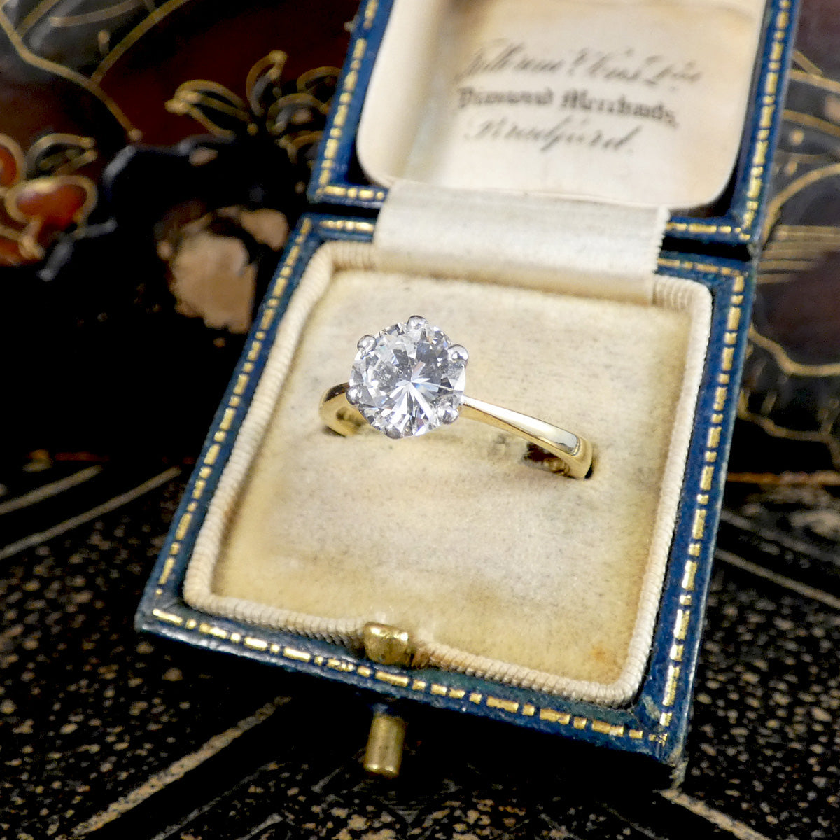 A vintage yellow gold ring with a large round-cut diamond set in a blue velvet ring box, photographed close-up.