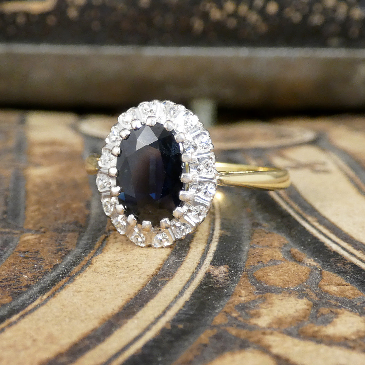 Ring with a blue gemstone and diamond halo on an ornate surface