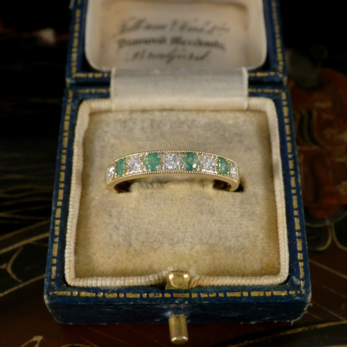 Gold ring with emeralds and diamonds in a blue jewelry box