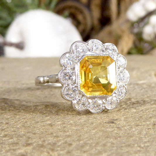 Art Deco-style ring featuring a stunning 2.10ct Asscher cut yellow sapphire, encircled by sparkling diamonds in a timeless cluster design.